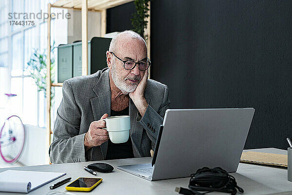 Geschäftsmann mit Kaffeetasse blickt im Studio auf Laptop