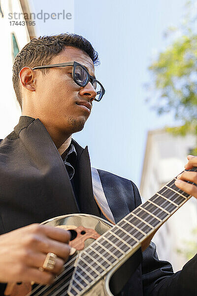 Männlicher Musiker mit Brille  der Gitarre spielt