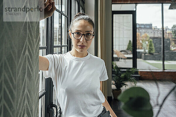 Mittlere erwachsene Geschäftsfrau mit Brille steht am Fenster im Büro
