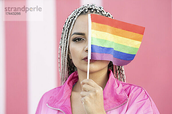 Junge Frau bedeckt Augen mit Regenbogenfahne an der Wand