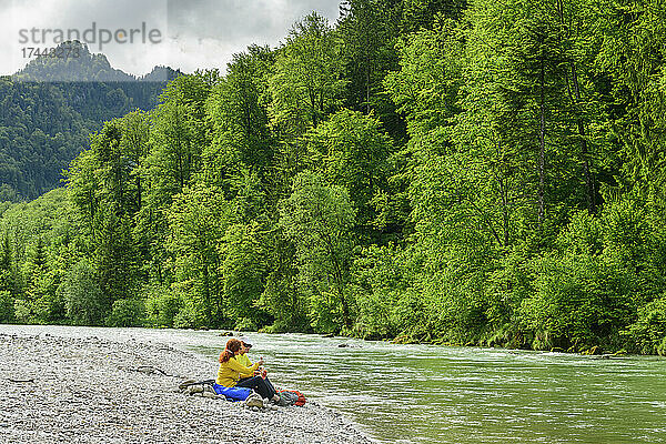 Reife männliche und weibliche Freunde sitzen im Urlaub am fließenden Fluss im Wald