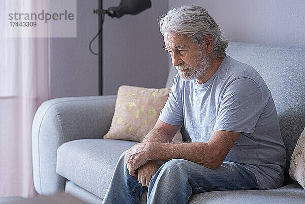 Einsamer älterer Mann sitzt zu Hause auf dem Sofa