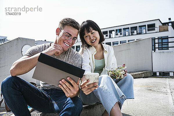 Männliche und weibliche Freunde teilen sich an sonnigen Tagen ein digitales Tablet und ein Smartphone