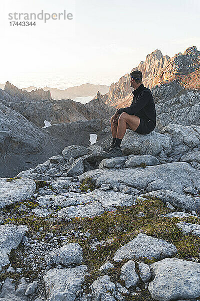 Junger Mann sitzt auf einem Felsen im Picos de Europe-Gebirge  Kantabrien  Spanien
