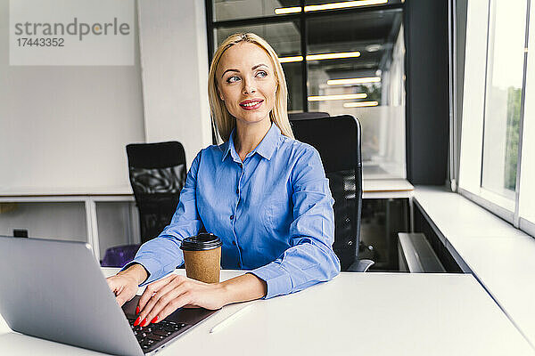 Blonde Geschäftsfrau mit Laptop sitzt am Schreibtisch im Büro