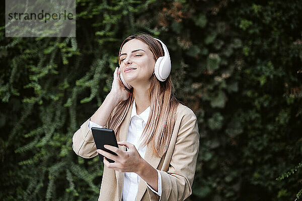 Berufstätige Frau hört mit geschlossenen Augen Musik über kabellose Kopfhörer von Pflanzen
