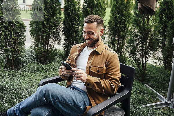 Lächelnder Geschäftsmann  der im Hinterhof Textnachrichten über sein Mobiltelefon sendet