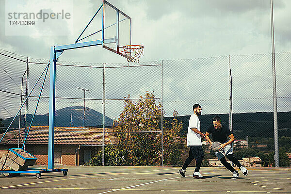 Mann verteidigt den Ball  während er mit einem Freund auf dem Sportplatz Basketball spielt