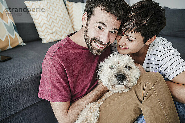 Lächelnder Mann und Frau sitzen mit Mischlingshund zu Hause