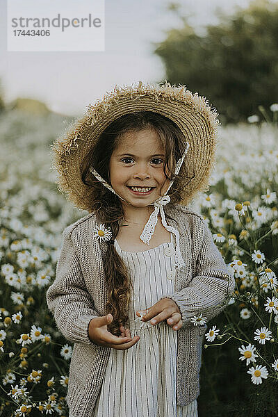 Lächelndes Mädchen mit Hut  das auf dem Blumenfeld steht
