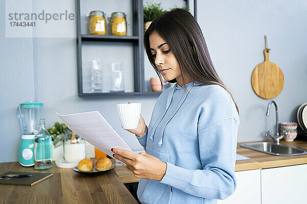 Schöne junge Frau liest Dokument  während sie zu Hause Kaffee trinkt