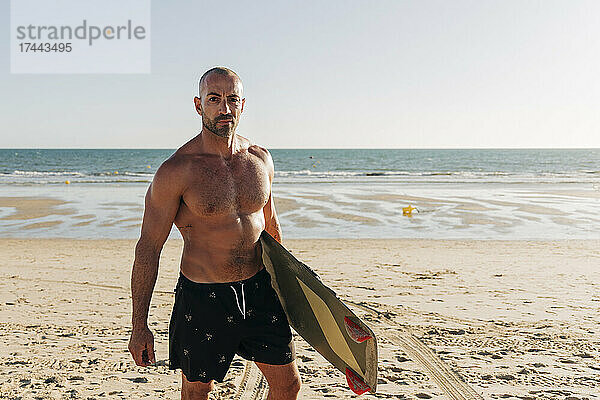 Hemdloser Mann hält Surfbrett am Strand