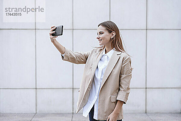Junge Geschäftsfrau macht Selfie mit Smartphone vor der Wand