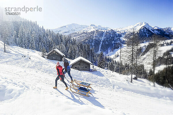 Paar zieht Rodel beim Spaziergang auf Schnee an sonnigen Tagen