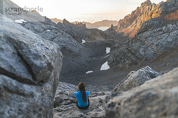 Junge Touristin blickt auf die Bergkette  während sie auf einem Felsen sitzt  Picos de Europe  Kantabrien  Spanien