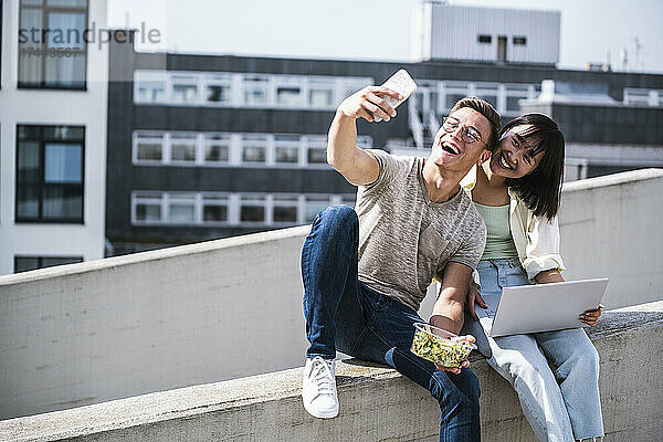 Fröhliche männliche und weibliche Freunde  die an sonnigen Tagen ein Selfie mit dem Smartphone machen