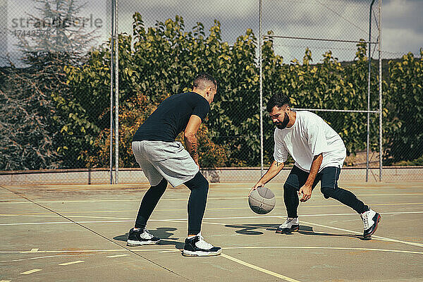 Männliche Freunde spielen Basketball auf dem Sportplatz
