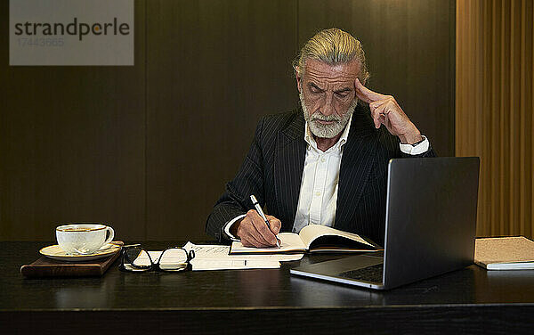 Geschäftsmann schreibt Tagebuch  während er am Schreibtisch im Hotel arbeitet