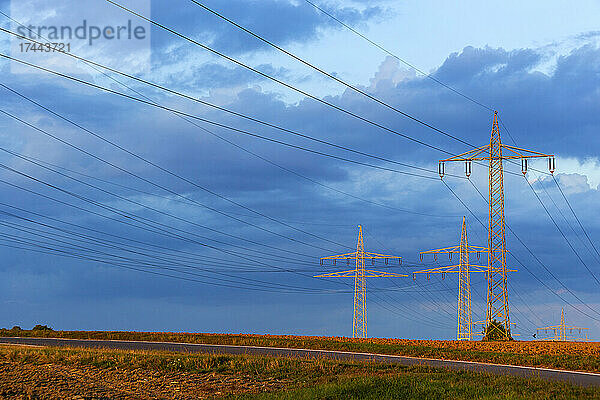 Strommasten stehen vor blauem bewölktem Himmel