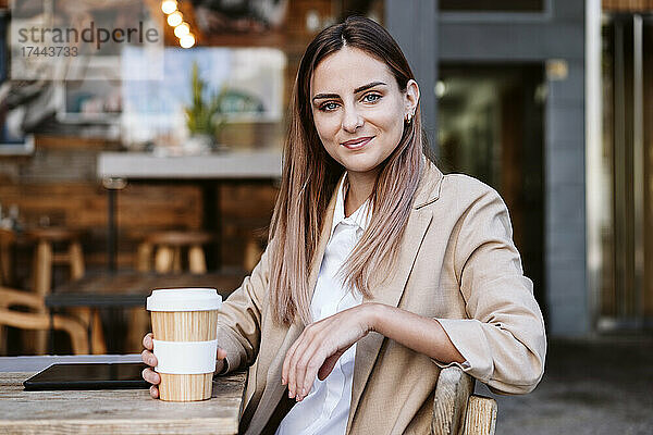 Geschäftsfrau mit Einwegbecher sitzt auf der Terrasse des Cafés