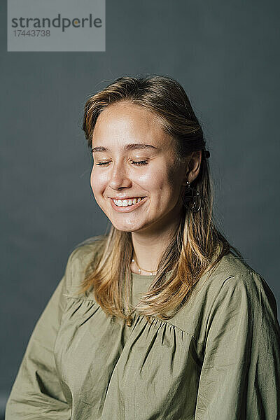 Lächelnde junge Frau mit geschlossenen Augen im Studio