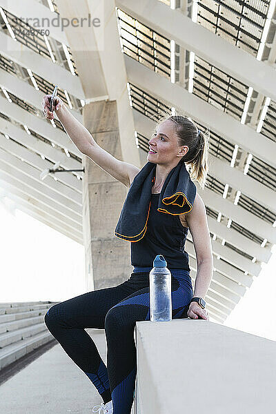 Sportlerin macht Selfie mit Smartphone an Stützmauer