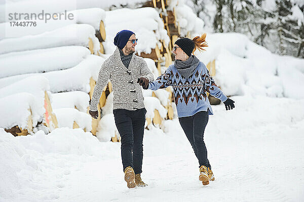 Mitte erwachsenes Paar in warmer Kleidung hält Händchen beim Gehen auf Schnee