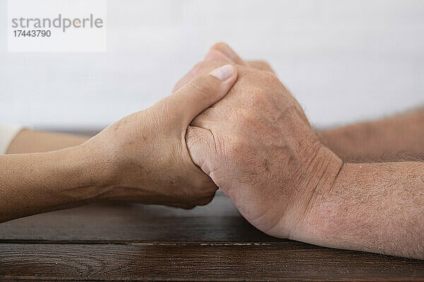 Älteres Paar hält Händchen am Tisch