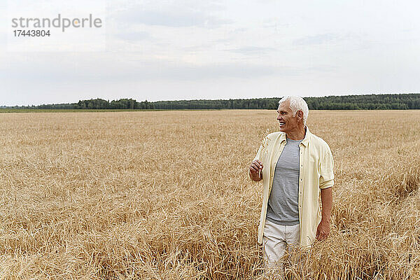 Lächelnder älterer Mann steht auf Weizenfeld