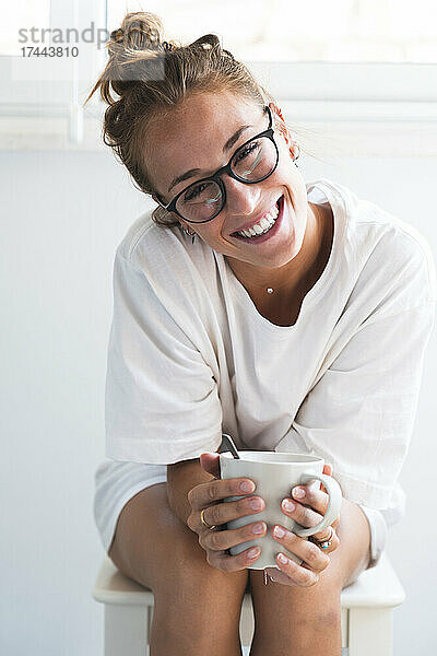 Schöne Frau mit Brille und Tasse in der Hand  während sie zu Hause sitzt