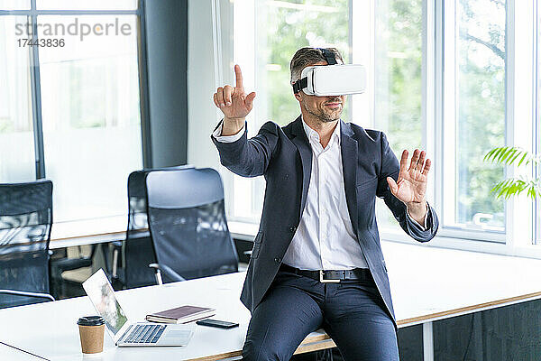 Männlicher Geschäftsprofi mit Virtual-Reality-Headset gestikuliert im Büro