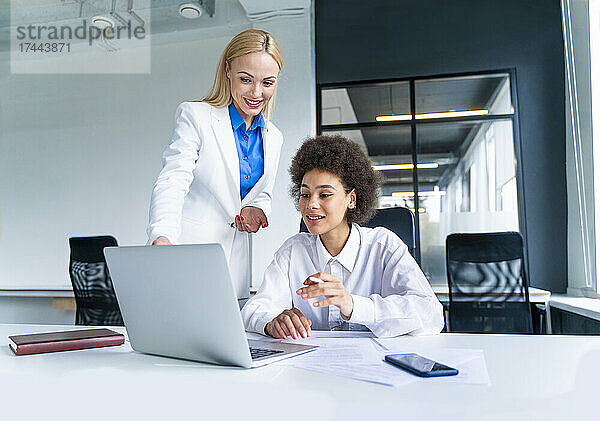 Lächelnde weibliche Geschäftsleute diskutieren am Laptop  während sie im Büro arbeiten