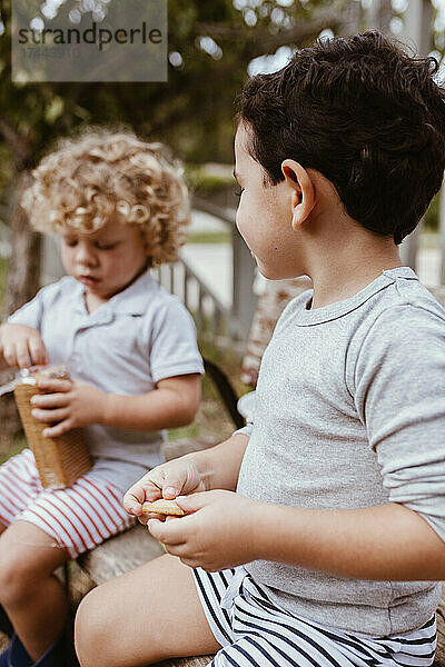 Jungen essen Kekse  während sie auf einer Bank sitzen