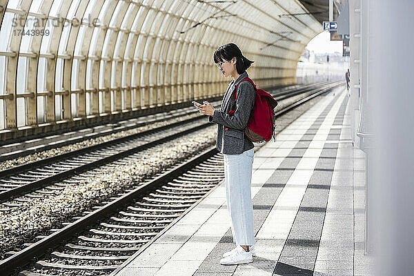 Teenager-Mädchen mit Rucksack benutzt Mobiltelefon am Bahnhof