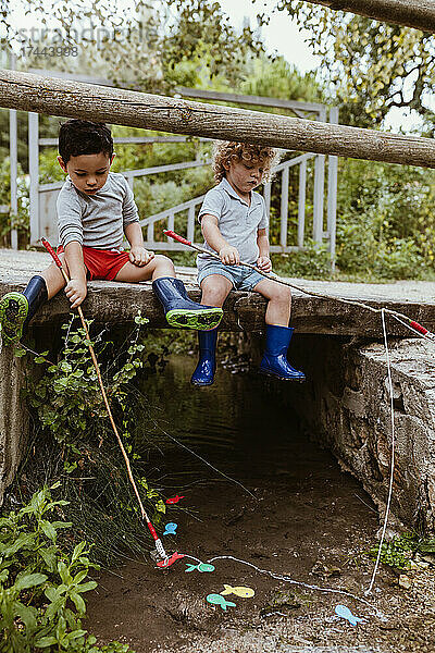 Jungen spielen mit künstlichen Fischen  während sie auf einer Fußgängerbrücke sitzen