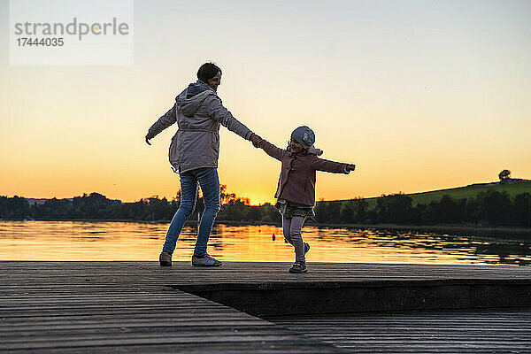Mutter und Tochter tanzen bei Sonnenuntergang auf dem Pier
