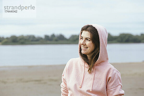 Lächelnde Frau mit Kapuzenshirt am Strand