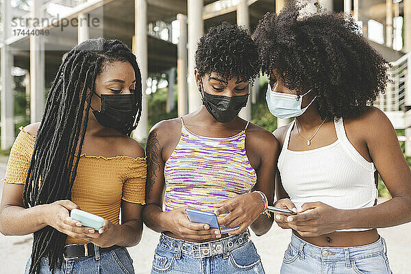 Junge Frau teilt während einer Pandemie ihr Smartphone mit Freundinnen