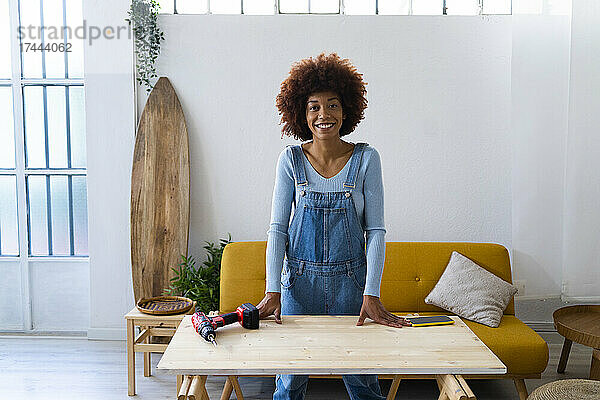 Rothaarige Afro-Frau steht am Tisch im Wohnzimmer