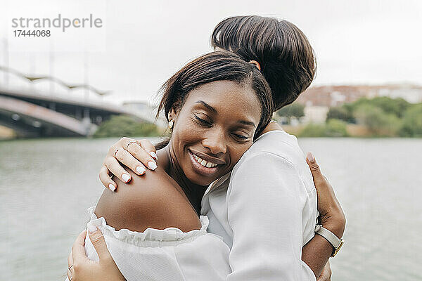Lächelnde Frau umarmt Freundin am Seeufer