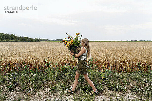 Mädchen hält einen Rainfarn-Blumenkorb in der Hand  während sie am Weizenfeld vorbeigeht