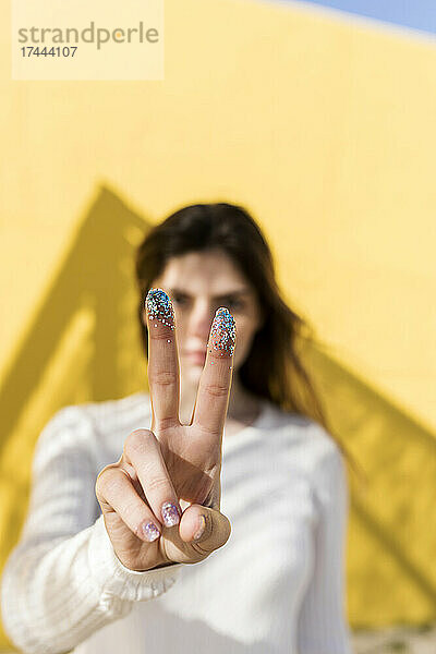 Frau gestikuliert mit Glitzer an den Fingern ein Friedenszeichen