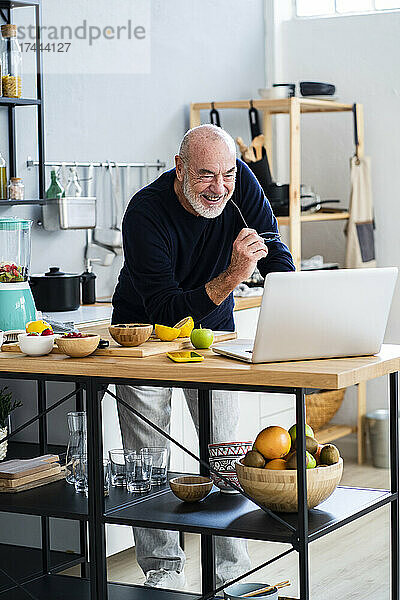 Fröhlicher älterer Mann benutzt Laptop an der Küchentheke
