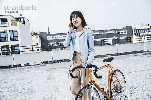 Lächelndes Teenager-Mädchen mit Fahrrad  das in der Stadt mit dem Handy telefoniert