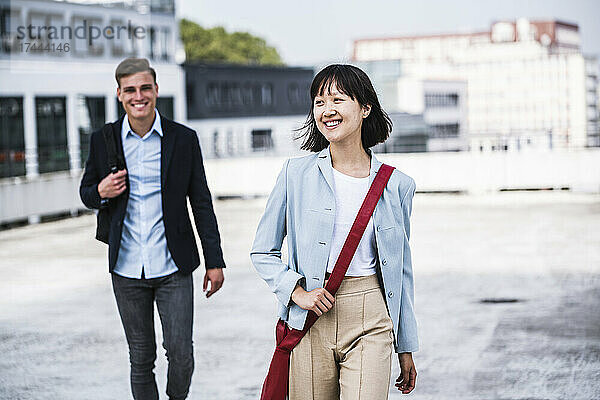 Geschäftsfrau mit Umhängetasche geht mit männlichem Kollegen auf dem Dach spazieren