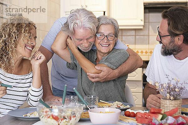 Ältere Frau umarmt Mann  während sie mit Familie am Esstisch sitzt