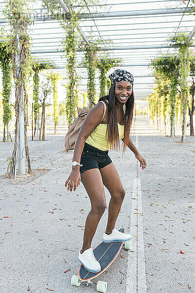 Frau mit Rucksack fährt Skateboard auf Fußweg
