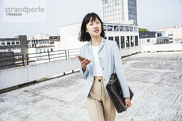 Geschäftsfrau läuft mit Mobiltelefon und Aktentasche auf dem Dach