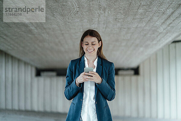 Lächelnde Freiberuflerin surft per Smartphone im Keller im Internet