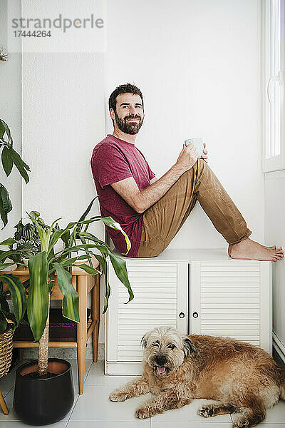 Mitte erwachsener Mann schaut weg  während er zu Hause mit einem Mischlingshund sitzt